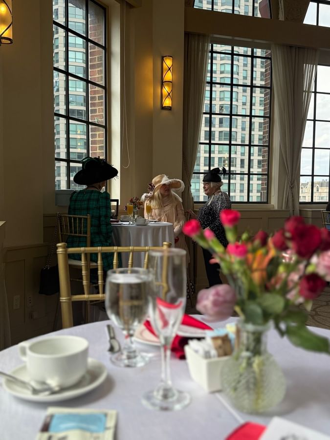 Guests in formal hats enjoying tea service by a large window at Warwick Allerton Chicago