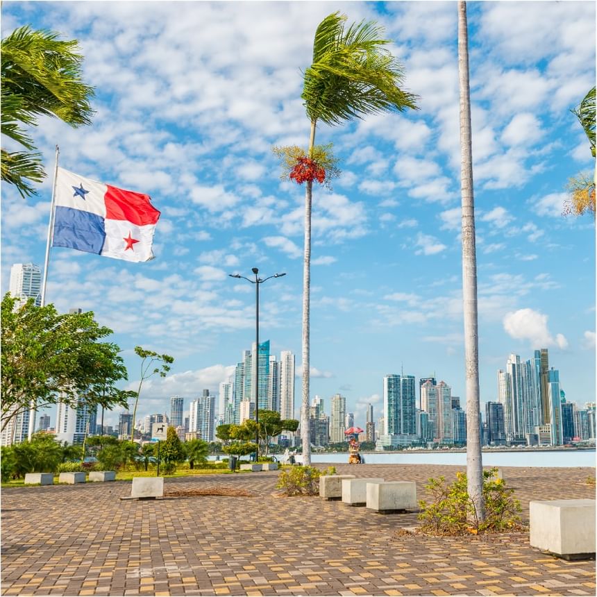 Bandera de Panamá ondea entre palmeras y bancos de piedra en un paseo cerca de Megapolis Hotel Panama