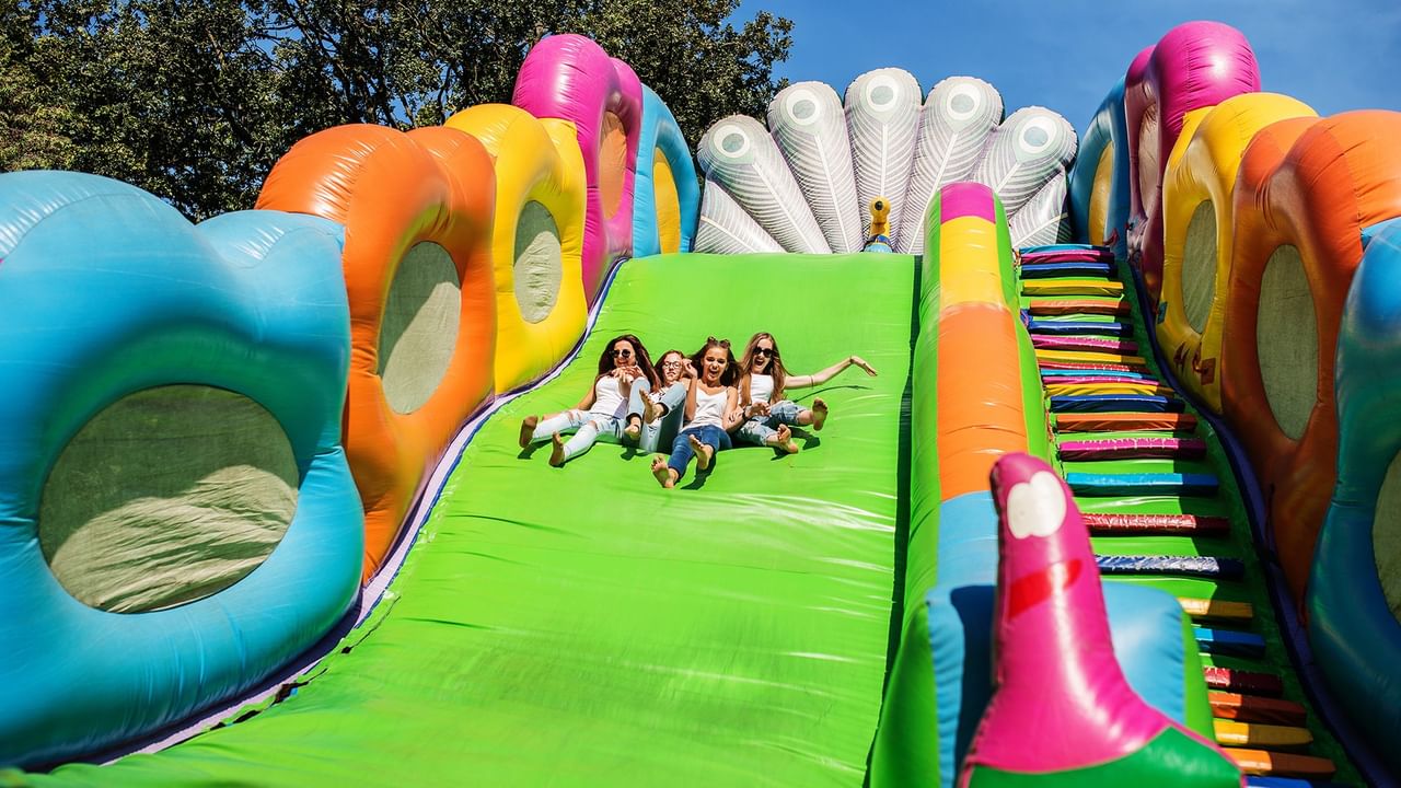 Four women slide down a large inflatable slide at Party In The Park.