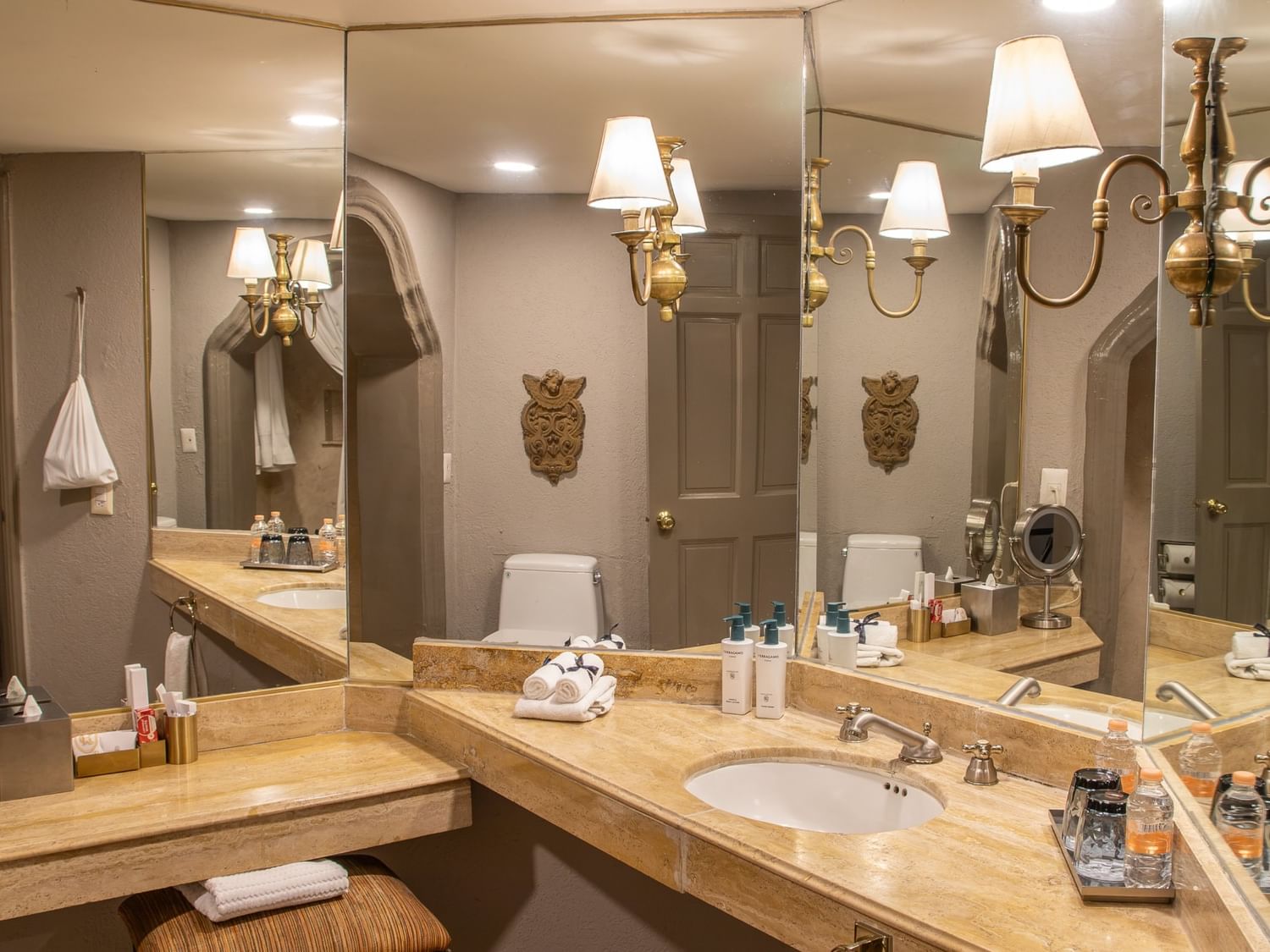 Baño elegante con tocador de mármol, espejos amplios y lámparas doradas en Quinta Real Guadalajara