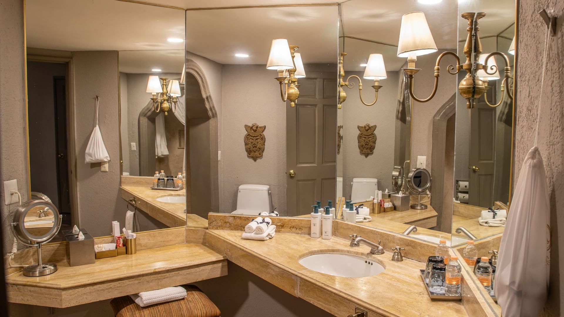 Baño elegante con tocador de mármol, espejos amplios y lámparas doradas en Quinta Real Guadalajara