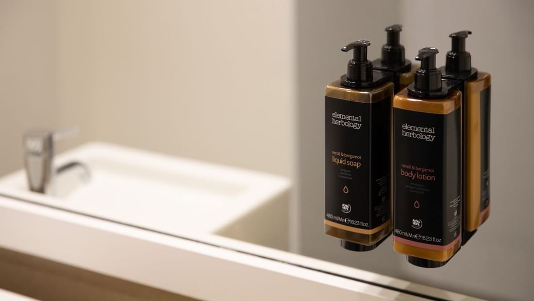Three bottles of liquid soap and body lotion mounted on a mirror above a sink.