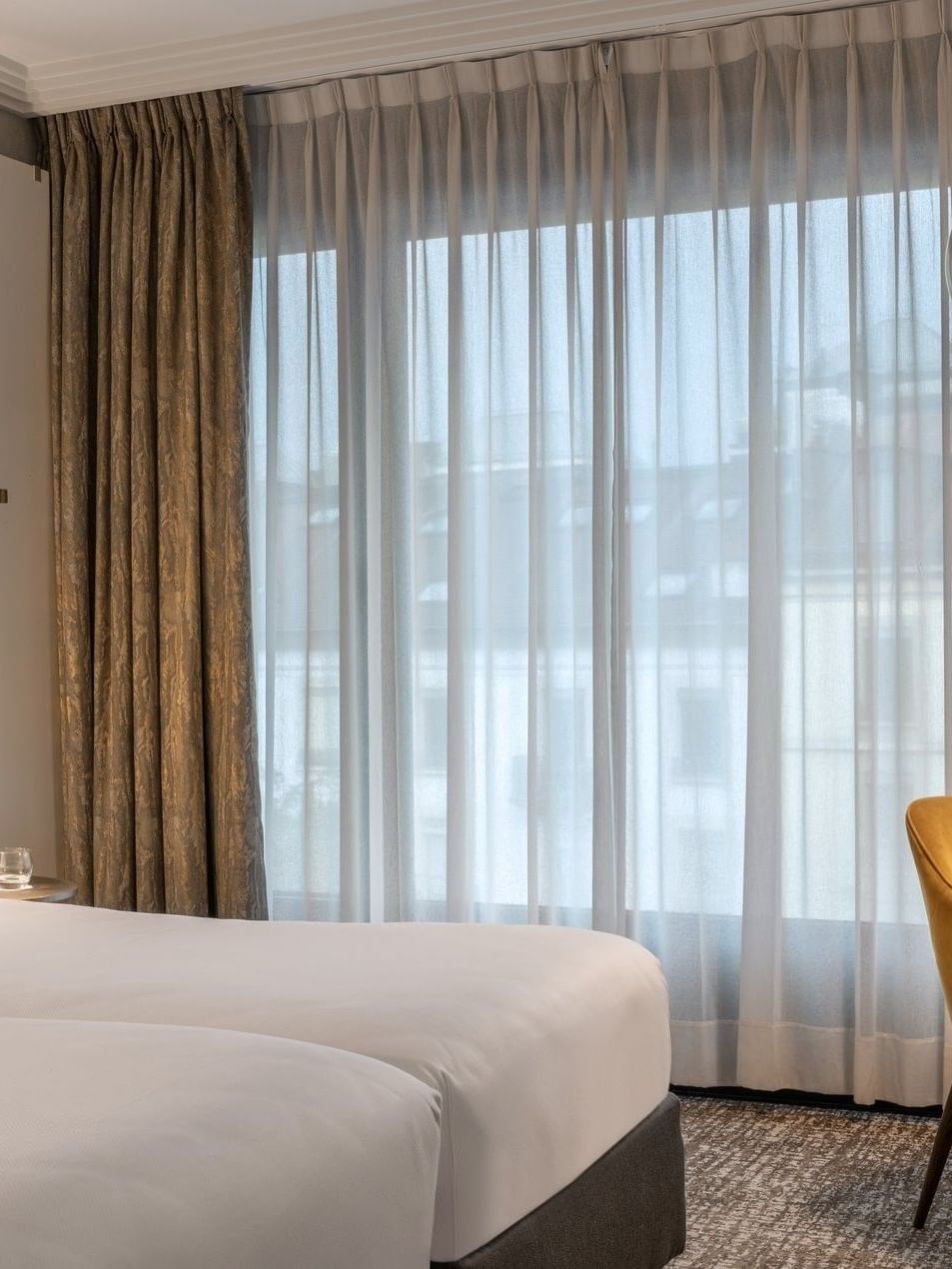 Twin beds by a yellow velvet armchair under a gold arched floor lamp near drapes in Classic Room at Warwick Geneva