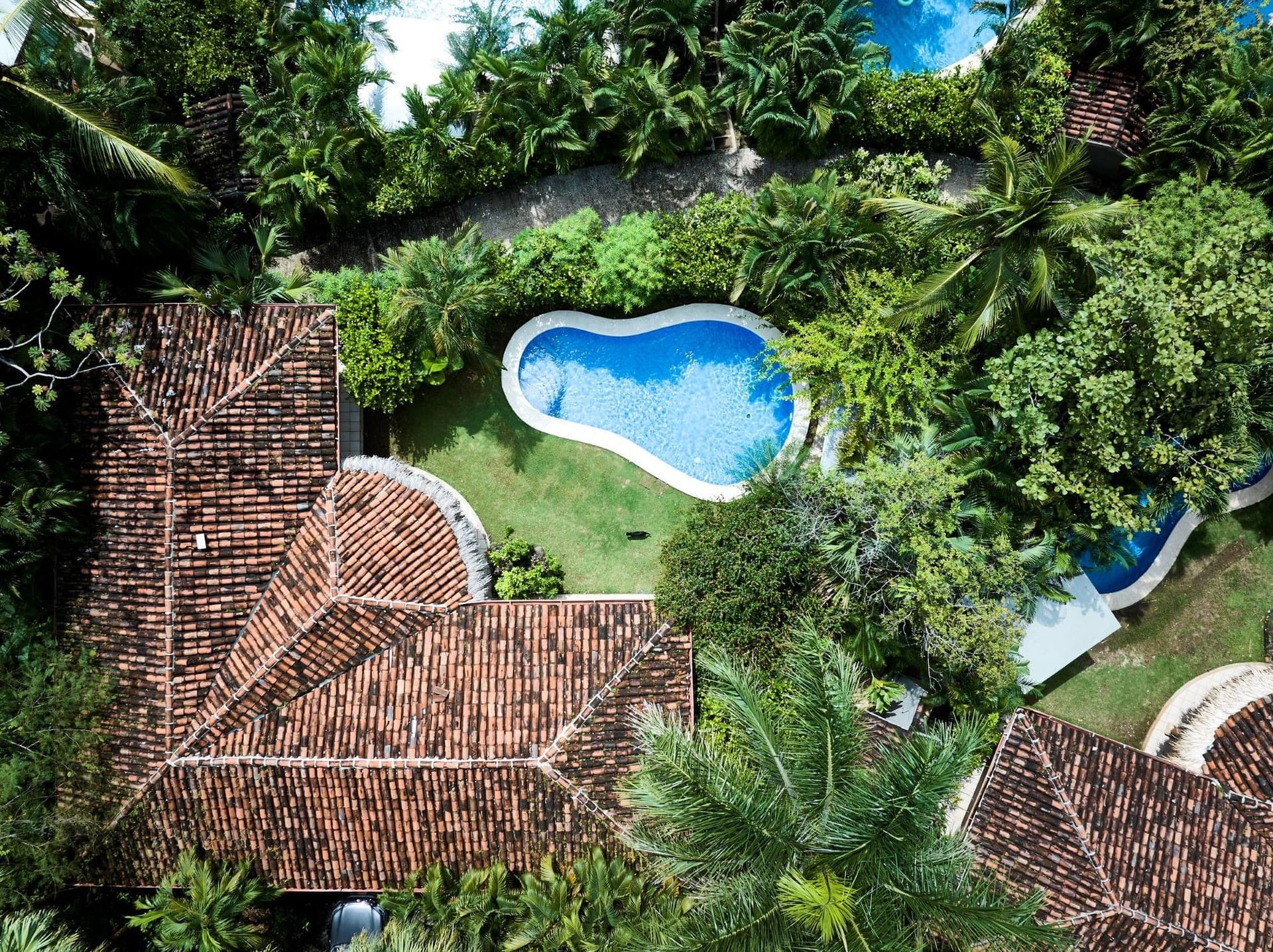 Birds-eye view of Cala Luna Boutique Hotel, showing tiled roofs and a private pool hidden in dense jungle flora