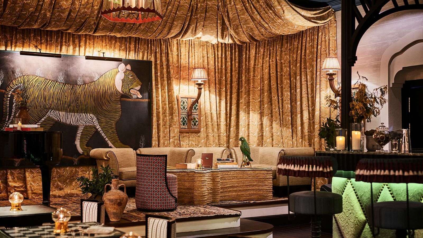 Opulent lounge with gold-draped curtains and a large tiger painting hanging behind a woven sofa at Marbella Club