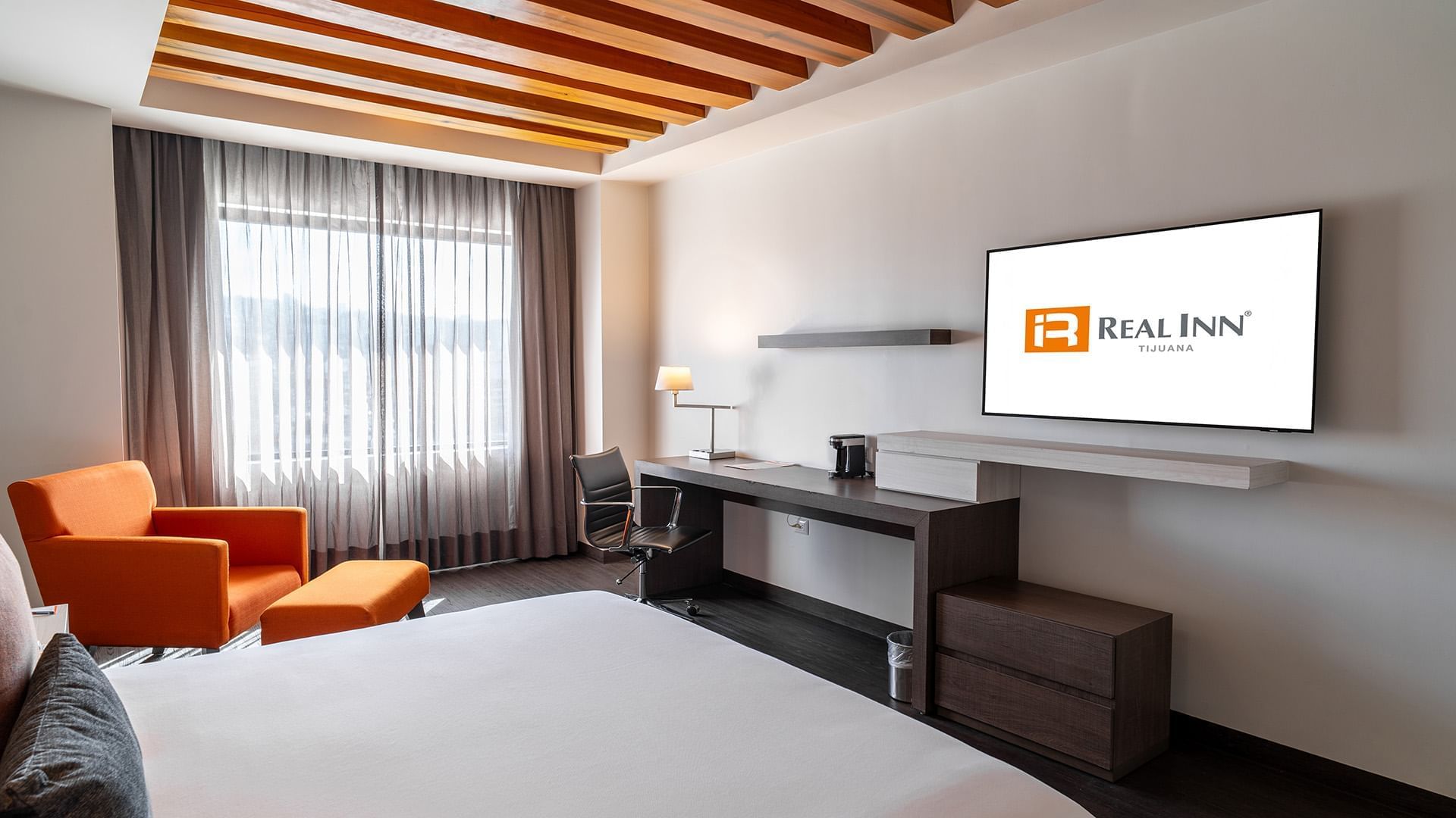 TV, work desk, and cozy lounge chair by the bed in the King Master Suite with wooden floors at Real Inn Tijuana