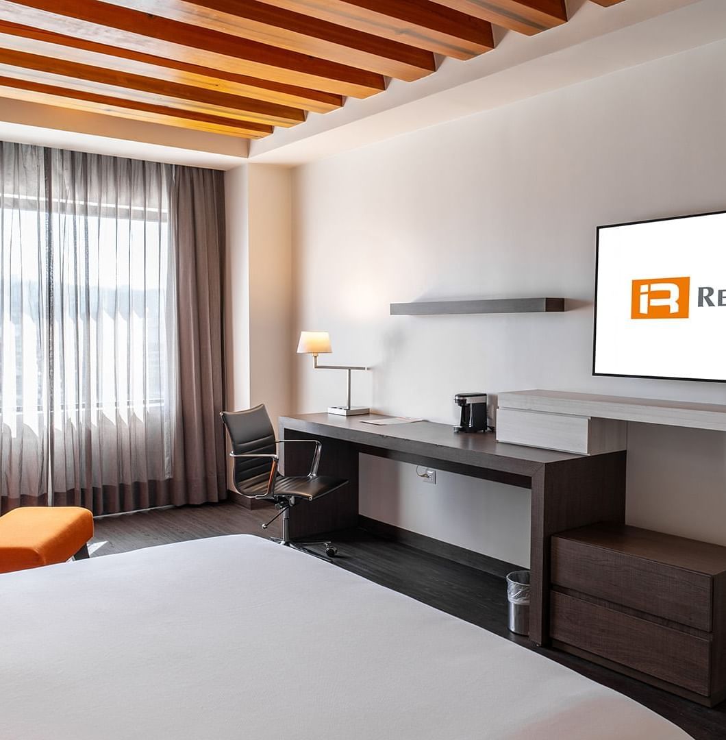 TV with work desk facing the bed and couch by the window in the King Master Suite at Real Inn Tijuana