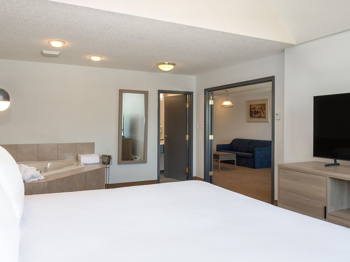 A hotel room with a large bed, flat-screen TV, couch, and a bathtub with a mirror.