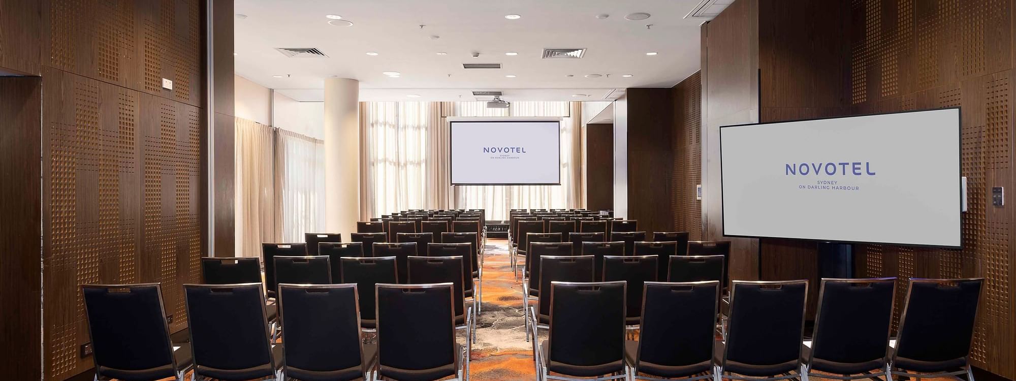 Theater-style table set-up facing the projector screen in The Hunter Room 1-4 at Novotel Sydney on Darling Harbour