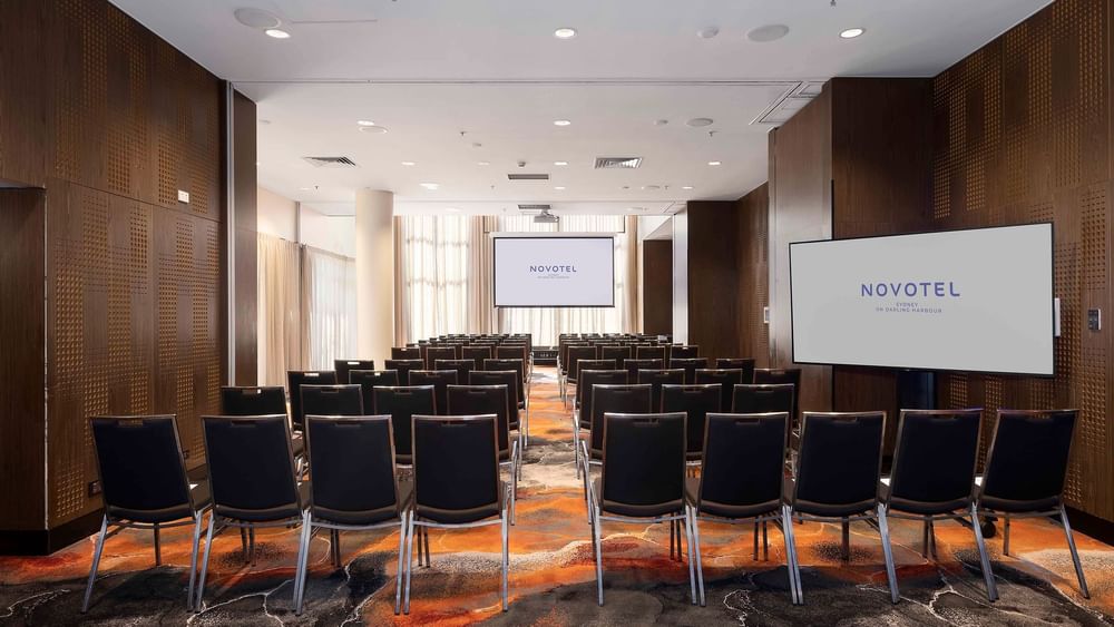 Theater-style table set-up facing the projector screen in The Hunter Room 1-4 at Novotel Sydney on Darling Harbour