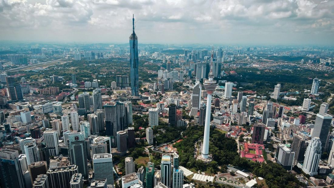 Merdeka 118 Aerial view of a city with numerous high-rise buildings and two prominent towers among green spaces.