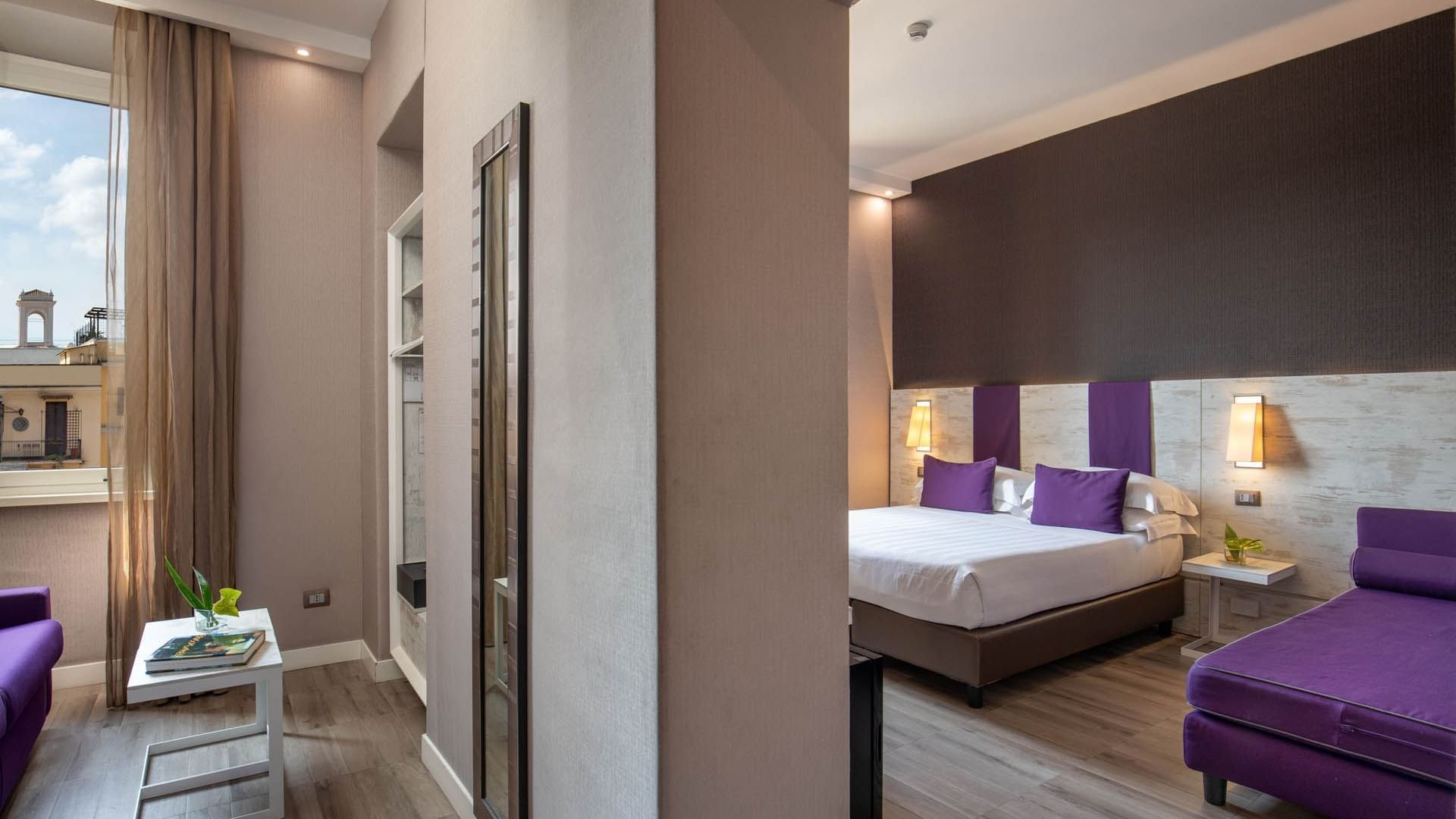 Separate living and bedroom areas in Junior Suite at The Guardian Hotel with a double bed, purple accents, and warm lighting