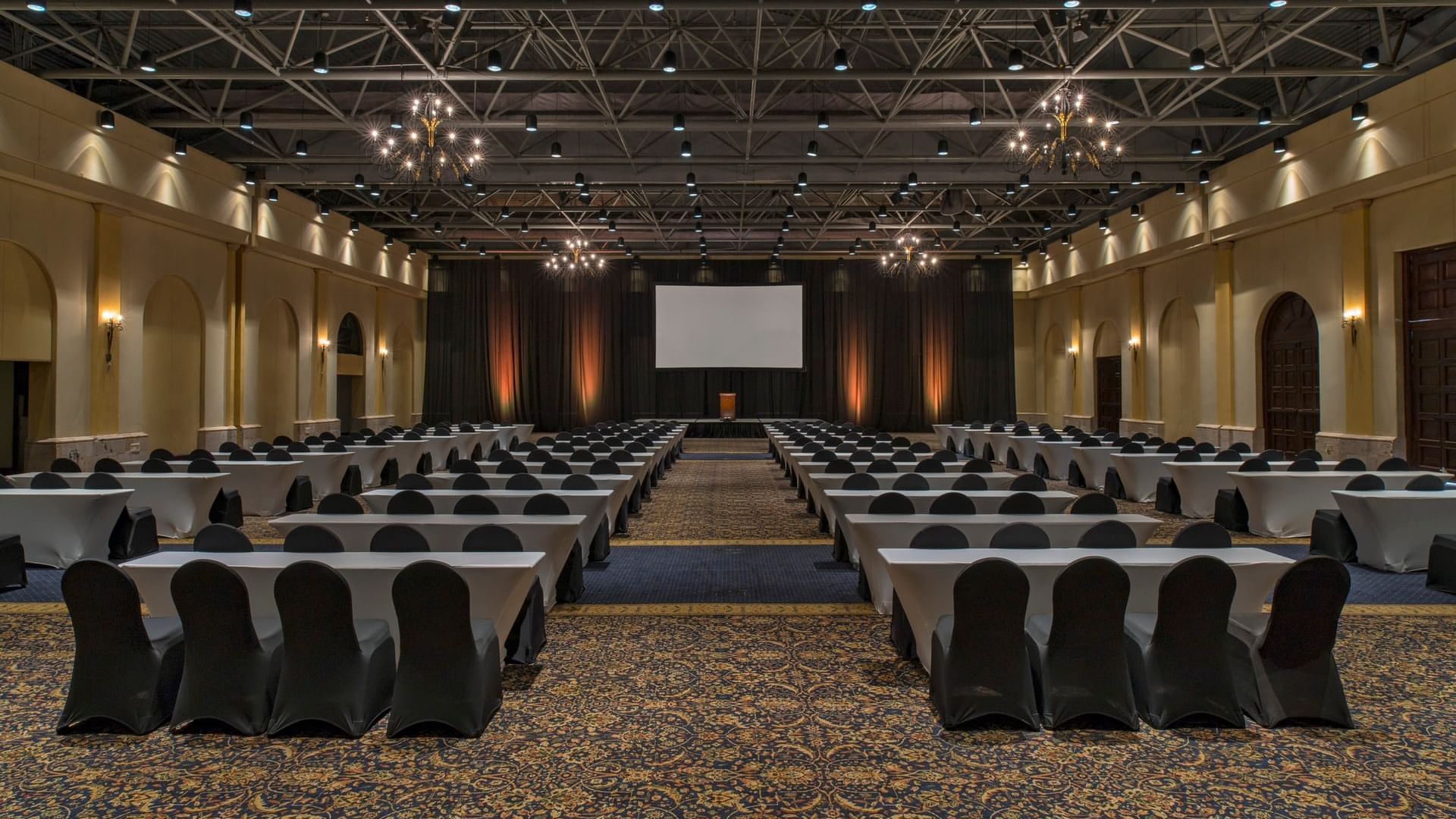 Salón Hacienda con sillas y mesas dispuestas cuidadosamente frente a una pantalla en Hacienda del Mar Los Cabos