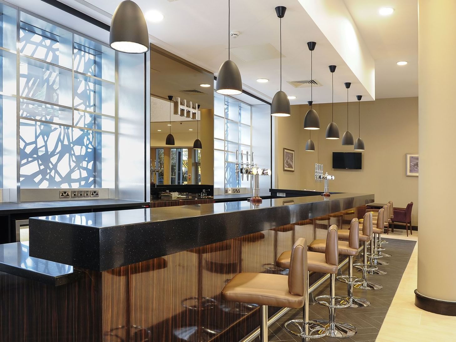Bar featuring a black countertop with brown stools and abstract designs on large windows at Heston Hyde Hotel