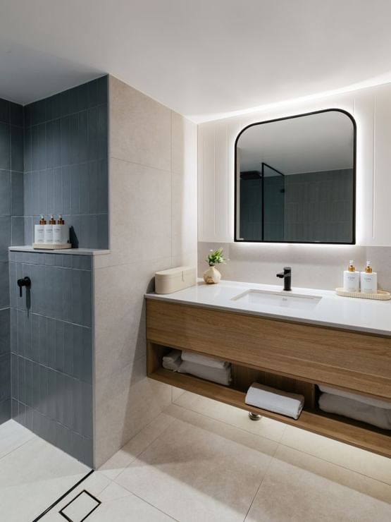 Ocean View King at Elysium Manly featuring a black faucet by pump bottles under a backlit mirror, with towels on a shelf