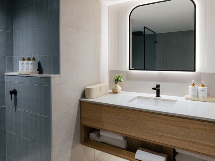 Ocean View King – Elysium Floor at Elysium Manly featuring a black faucet by Bottles under a mirror, with towels on a shelf