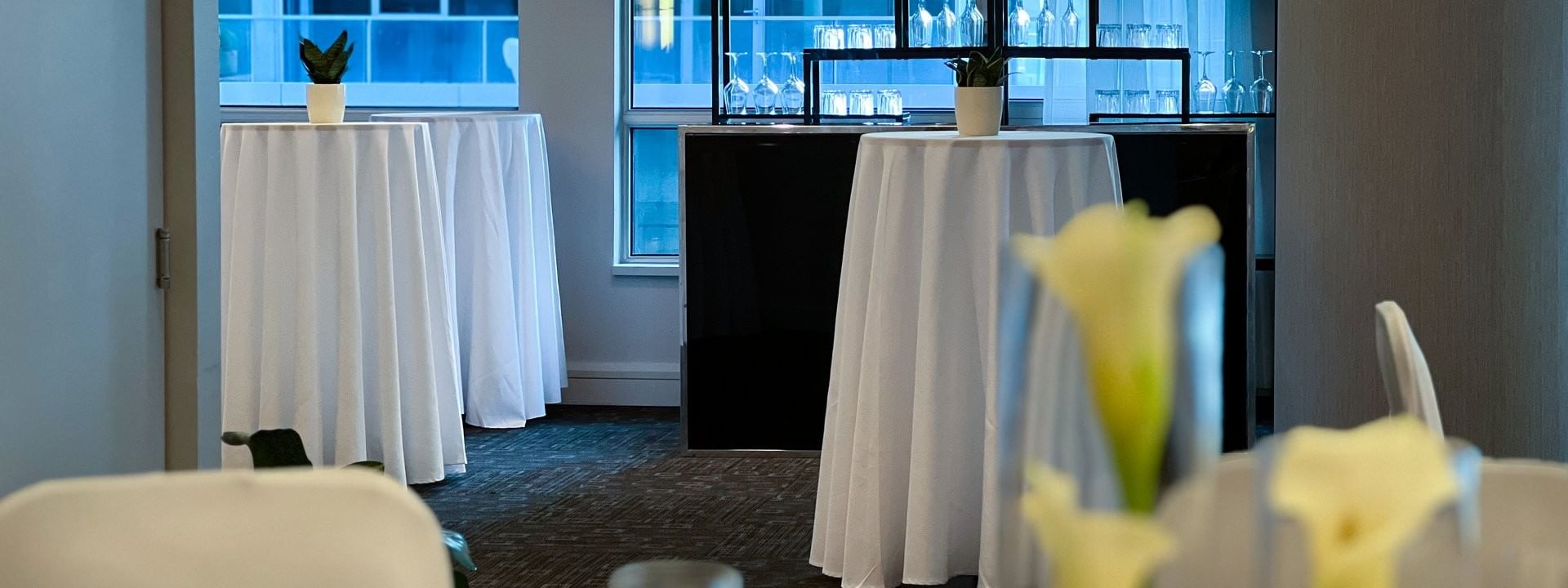 High-top tables with small green plants by a glass shelving unit in Ballroom at Warwick Le Crystal Montreal