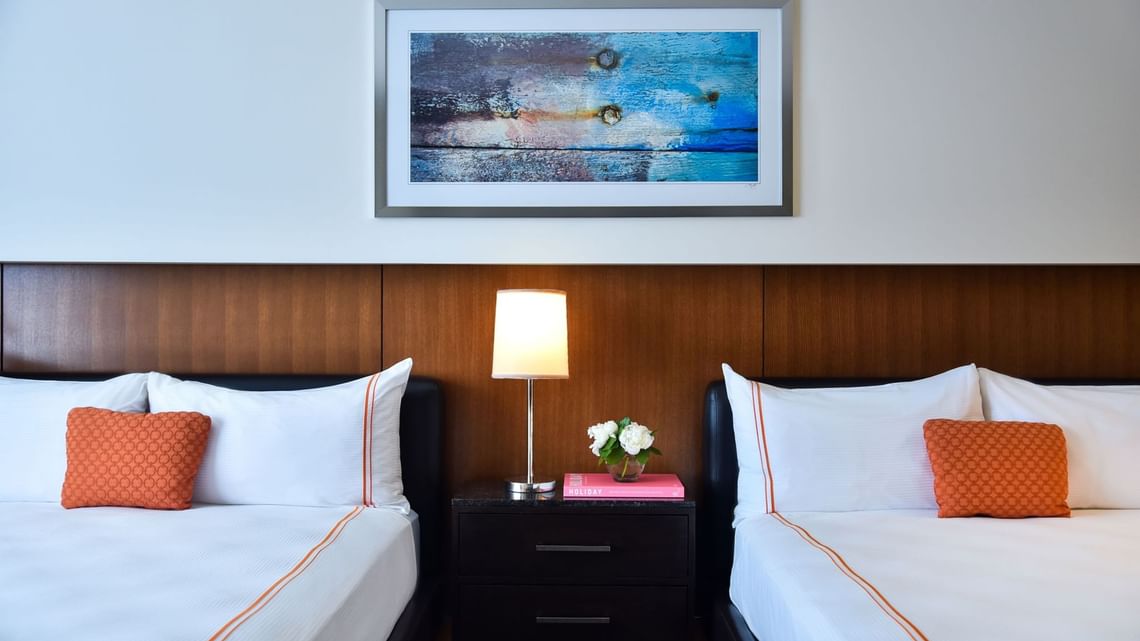 Two beds with orange pillows and a nightstand lamp