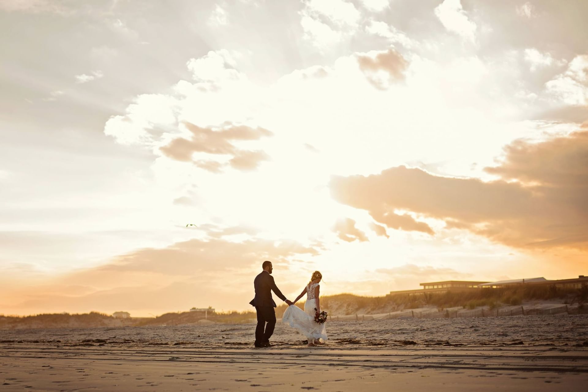 Newlywed couple holds hands and walks along the beach near our Avalon wedding venue