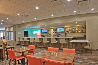 Well-stocked bar and lounge area with wooden tables and glowing neon signs in Bottom's Up Lounge at Buffalo Bill Village