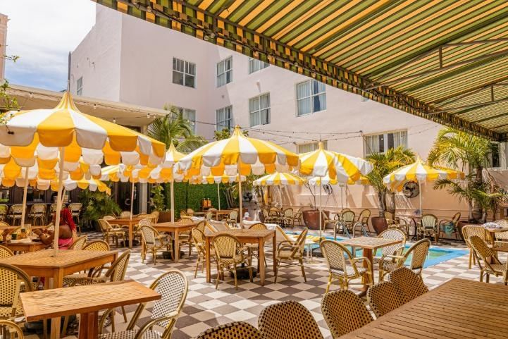 A poolside seating area with wooden tables, wicker chairs, and yellow and white umbrellas.