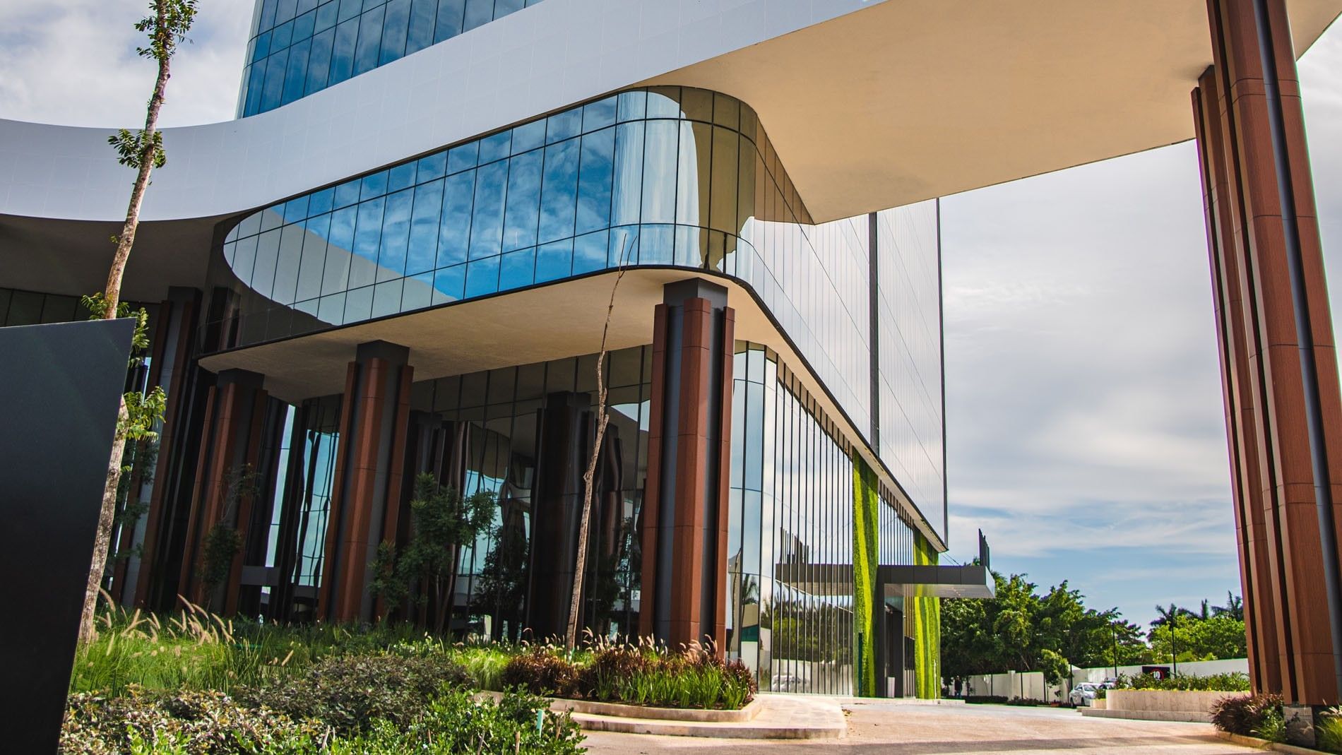 Modern architectural entrance showing glass walls and sleek pillars with greenery at Camino Real Merida