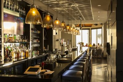Sleek bar stools by a long counter under glowing glass pendants in 1809 Restaurant & Bar at Rodd Miramichi River
