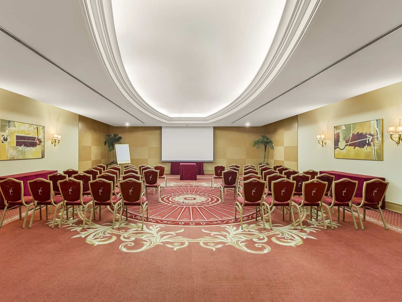 Sala de reuniones con sillas en círculo, proyector y mesas cubiertas con manteles rojos.