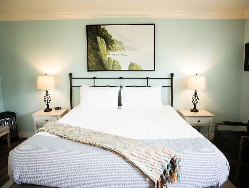A serene bedroom with a large bed, two nightstands with lamps, and a painting above the bed.