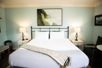 A serene bedroom with a large bed, two nightstands with lamps, and a painting above the bed.