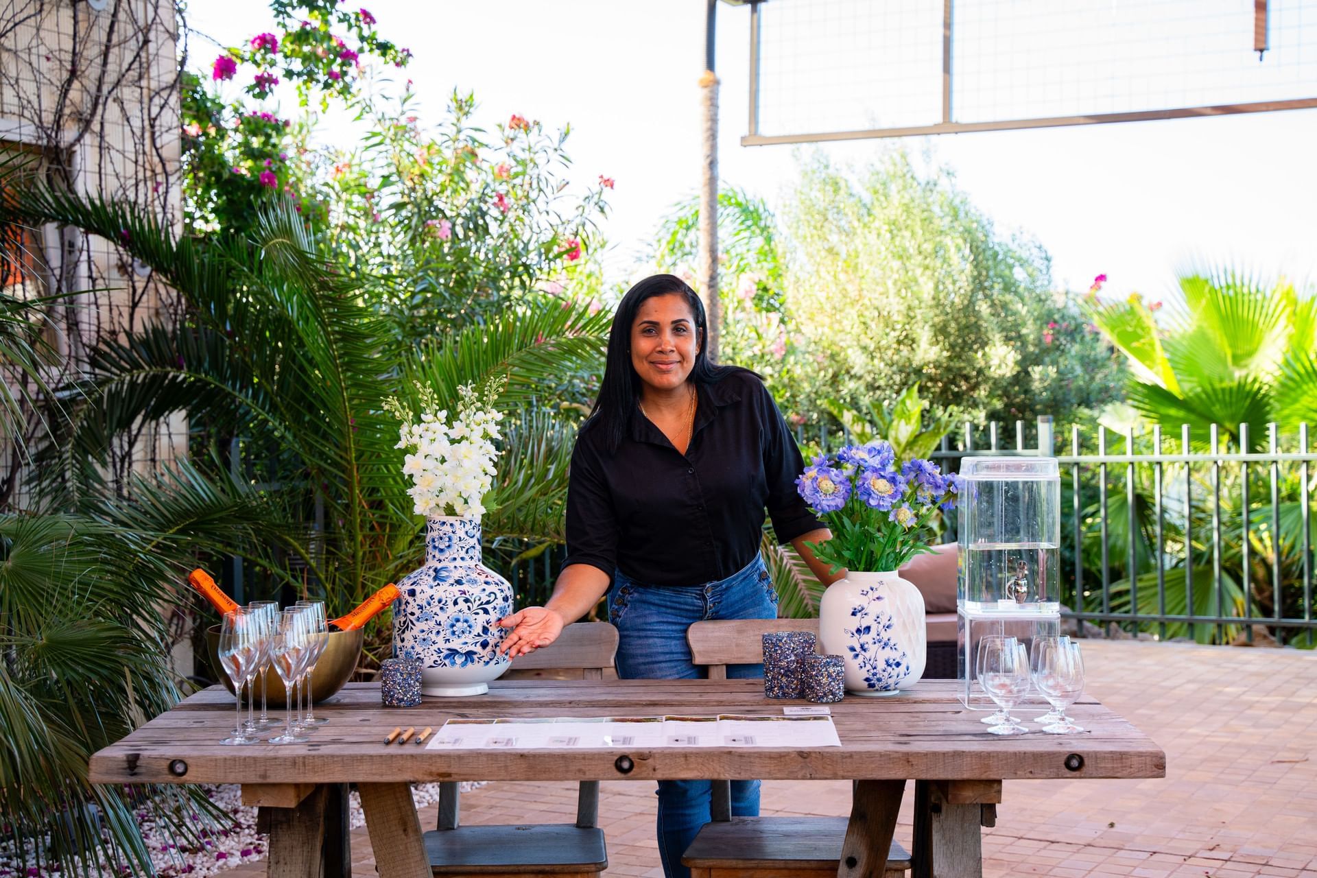 Vrouw die naast een elegant gedekte buitentafel met bloemstukken en glaswerk staat bij Golden Rock Resort