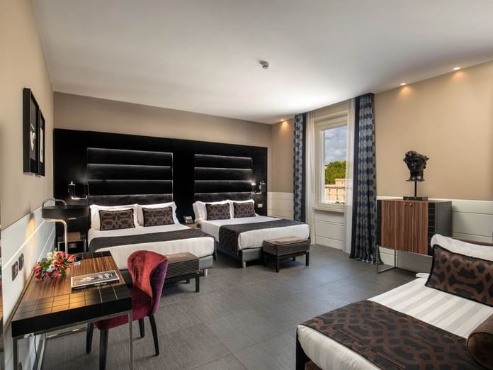 Two beds by the window with a work desk and seating in Open Suite at The Glam Hotel