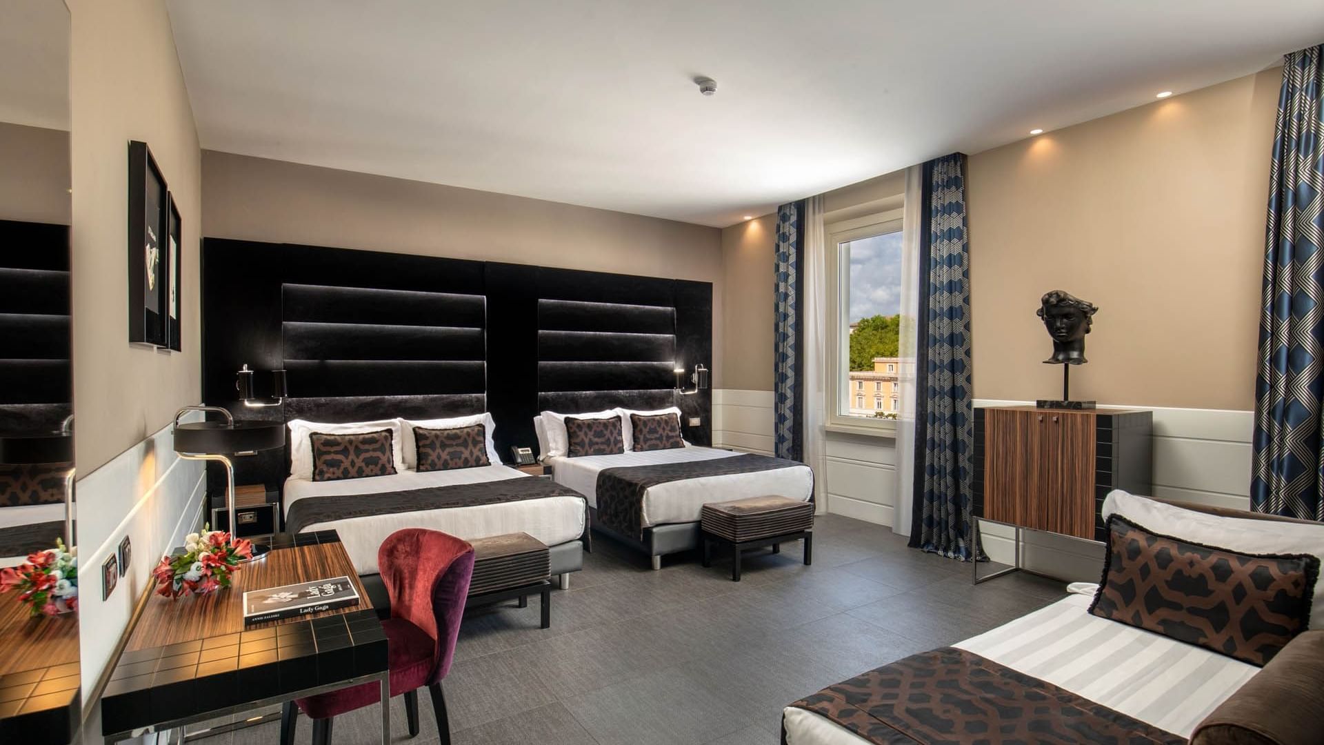 Two beds by the window with a work desk and seating in Open Suite at The Glam Hotel