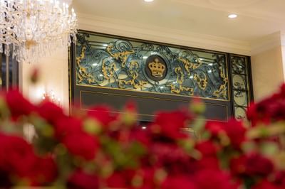Gold-accented wrought iron panel featuring a royal crown, with a backdrop of lush red roses at Grand Emperor Hotel