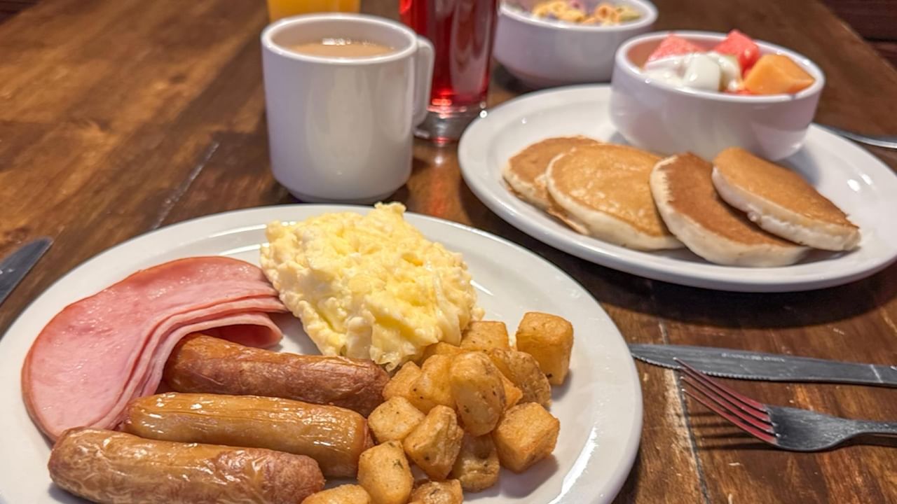 Two plates of breakfast food with ham, eggs, sausage, and hash browns.