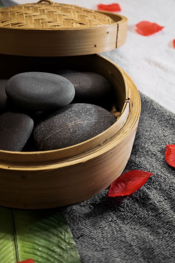 Smooth spa stones in a bamboo steamer by red petals on a gray towel at the Arlington Resort Hotel & Spa