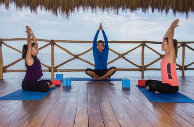 Tres personas practican yoga sobre esterillas frente al mar en el Sunset Plaza Beach Resort, uno de los mejores hoteles con vistas a la playa en Puerto Vallarta