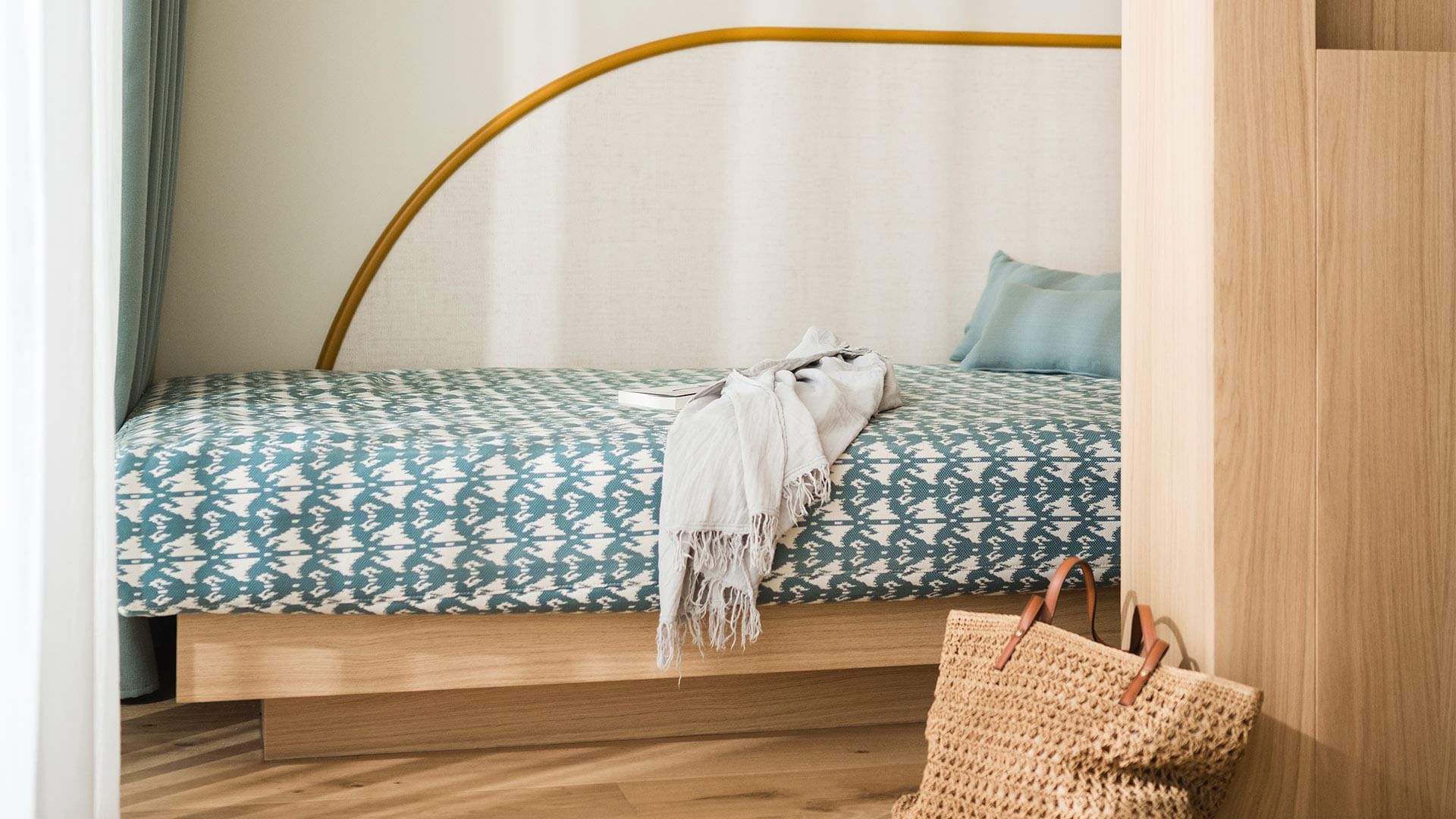 Wooden daybed with blue and white patterned bedding, a blue pillow, and a beige blanket.