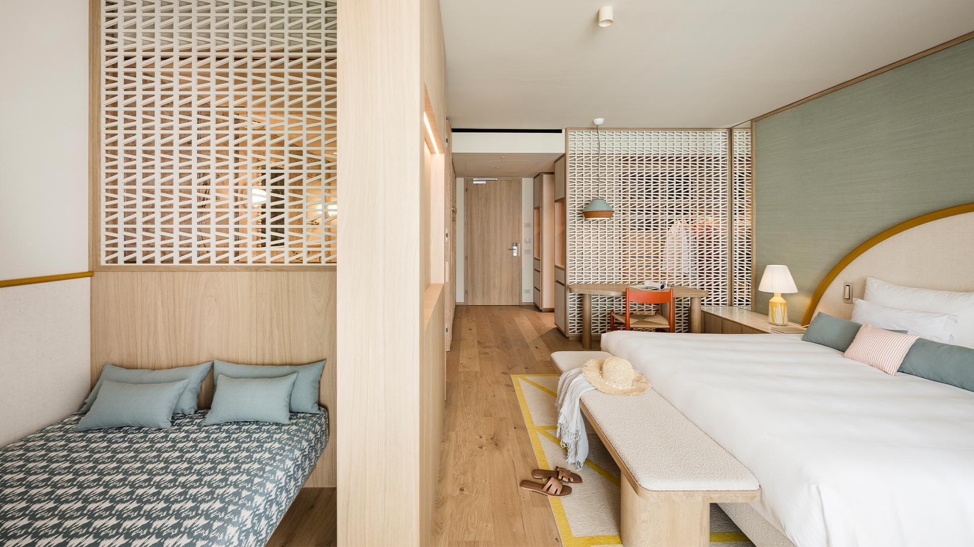 Interior of a modern hotel room with two beds, wooden floors, and a lamp on the side table.