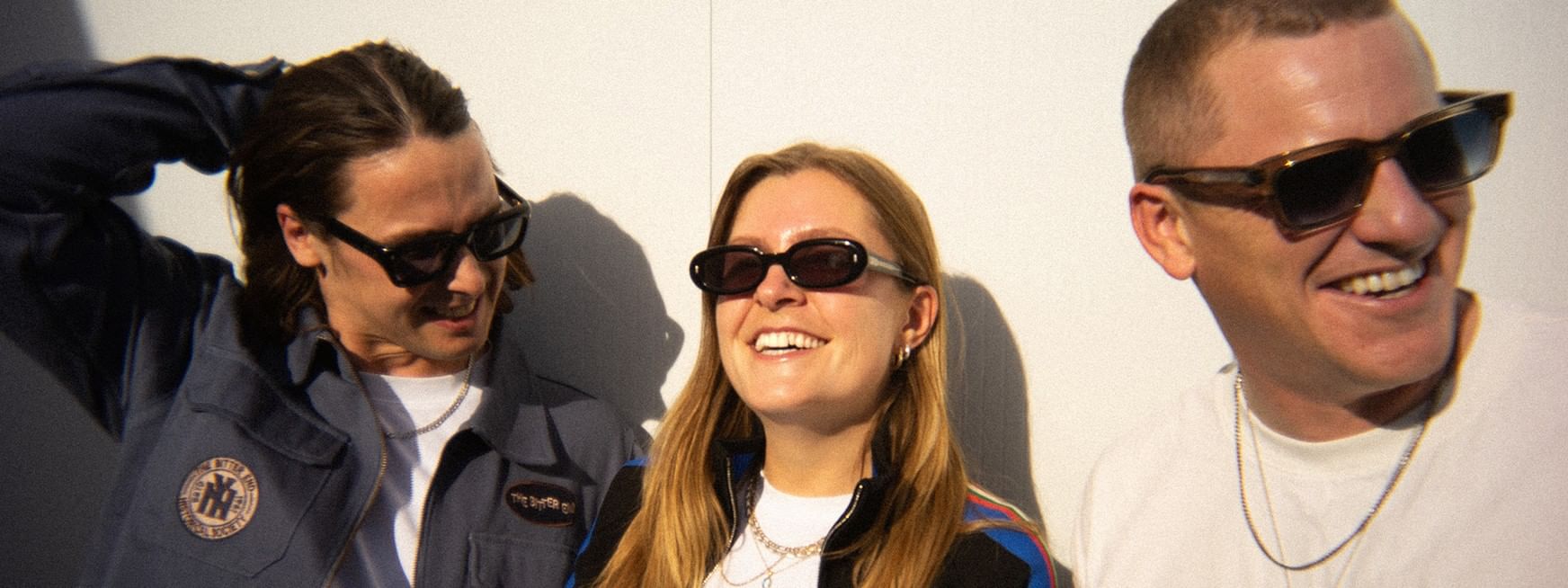 Three smiling individuals wearing sunglasses stand together for a photo for the Jungle Tour 2027.