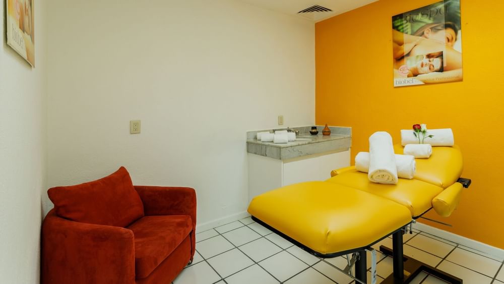 Treatment room showing a massage bed and a yellow accent wall at Camino Real Aeropuerto Mexico