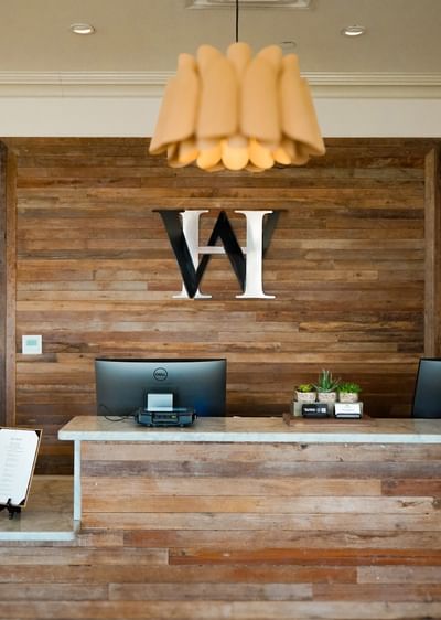 A wood-paneled lobby at The White House Hotel with a marble desk, petal light, and a large black and white logo