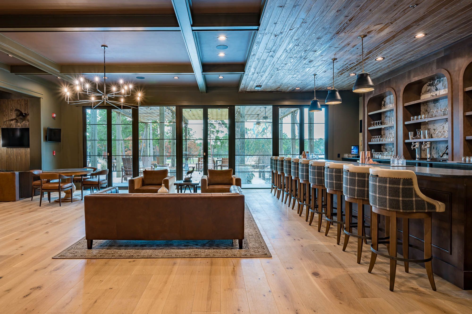 Lounge area with large couch, dining table, and bar with stools, illuminated by chandelier and pendant lights.