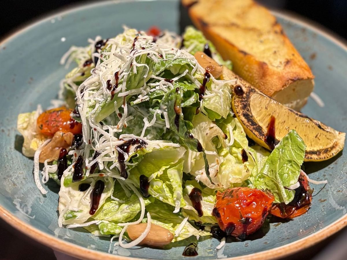 A blue plate holds a salad with lettuce, tomatoes, and croutons, topped with dressing and grated cheese.