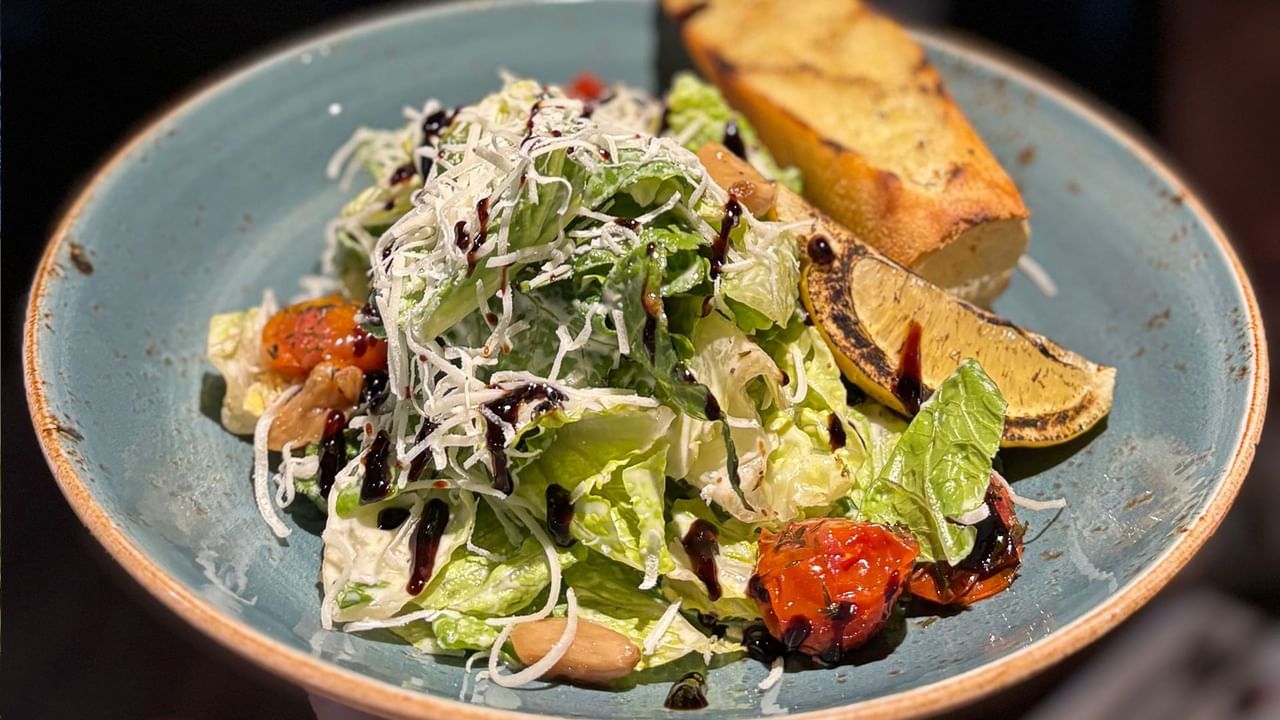 A blue plate holds a salad with lettuce, tomatoes, and croutons, topped with dressing and grated cheese.