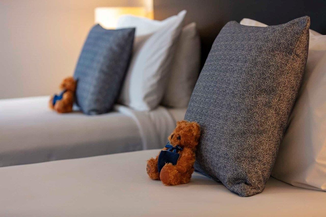 Close-up of two twin beds with cozy cushions and small welcome teddy bears in Two Bedroom Apartment at The Sebel Brisbane