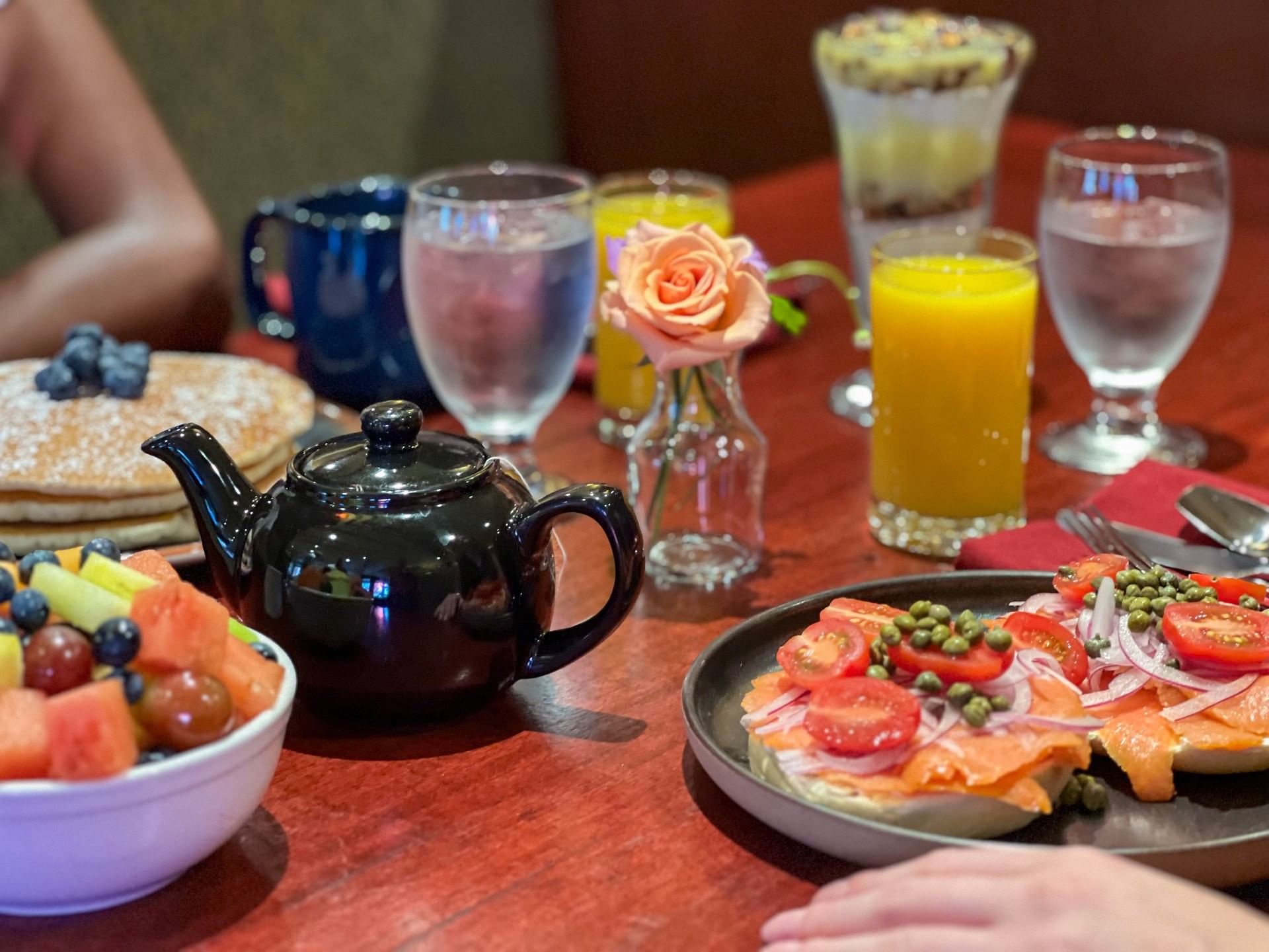 Breakfast table spread featuring salmon bagels, fresh fruit bowl, a teapot, orange juice, and pancakes at Margaux Restaurant