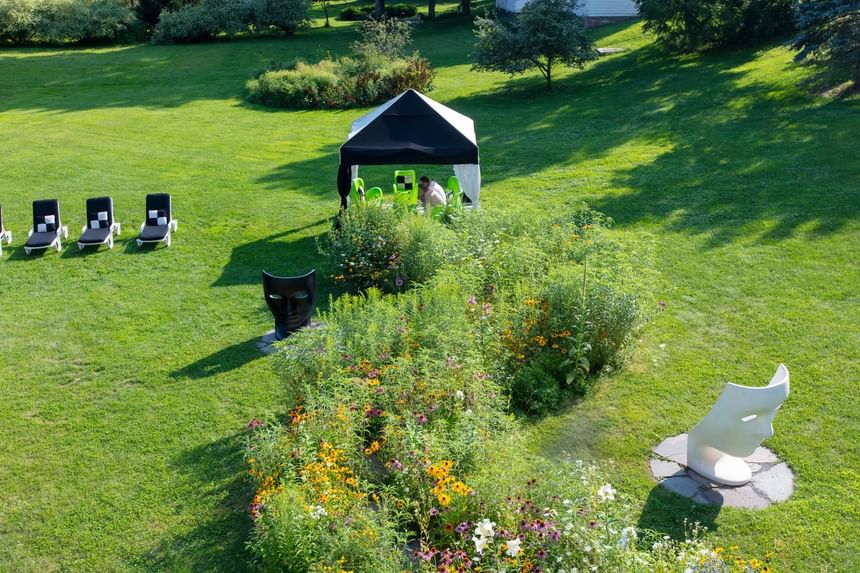 Lush green lawn features lounge chairs, colorful flowers, a white sculptural and a tent at The Roxbury
