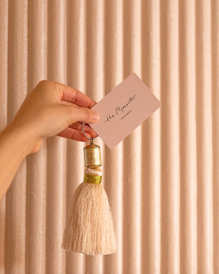 Hand holding the stylish, custom pink key card and tassel against a textured pink wall at The Plymouth Hotel South Beach