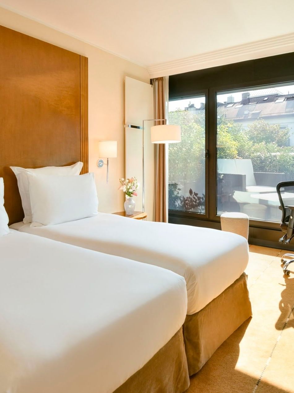 Twin beds by a wooden desk and a rolling chair in Deluxe Terrace Room at Warwick Geneva